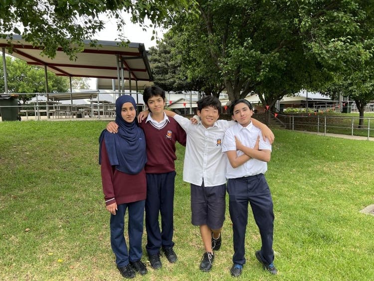 Four students standing on grass area of playground